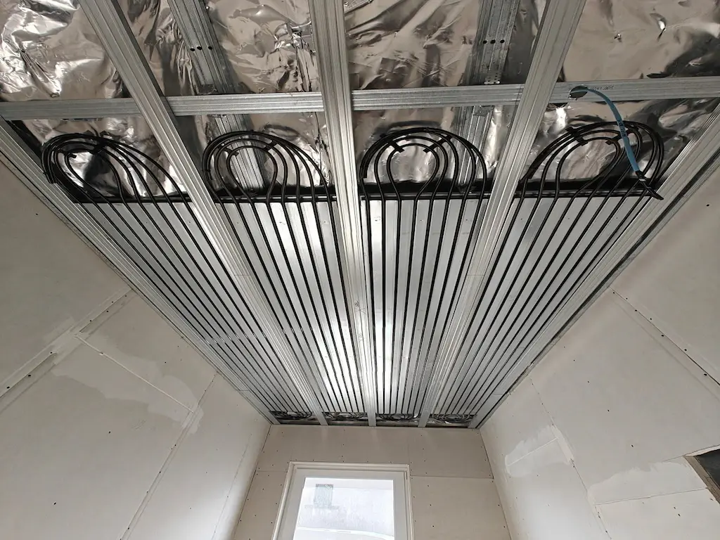 A Heat Builder Kft. által kivitelezett mennyezetfűtési rendszer telepítése; a képen a gipszkarton vázszerkezet közé precízen beépített fekete hűtő-fűtő csőregiszterek láthatóak hőtükör fóliával kiegészítve.