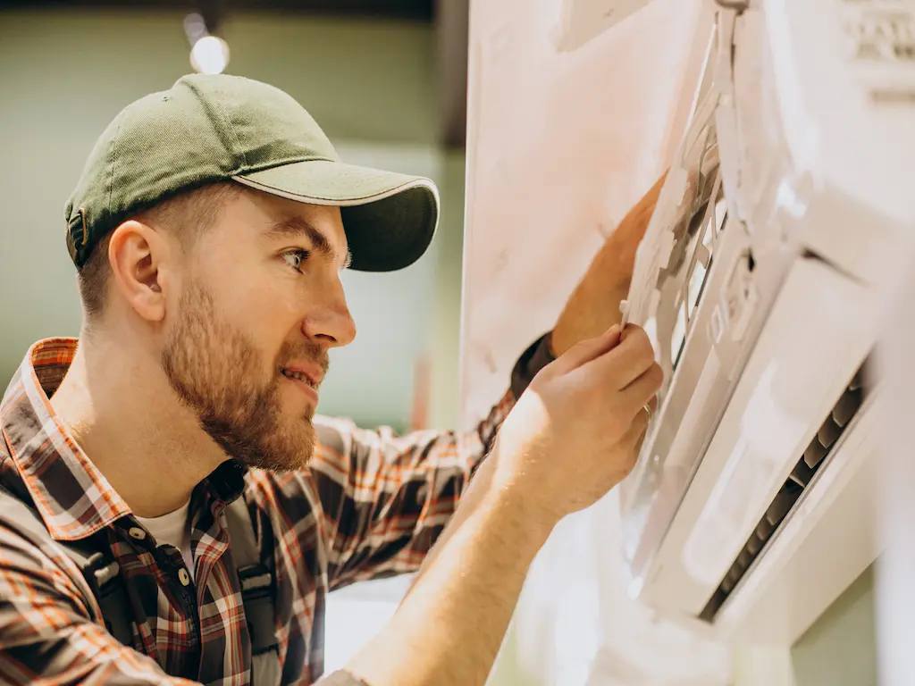 A Heat Builder Kft. szakembere precíziós karbantartást végez egy oldalfali légkondicionáló egységen; a képen a beltéri egység szűrőinek és előlapjának szakszerű beállítása látható.